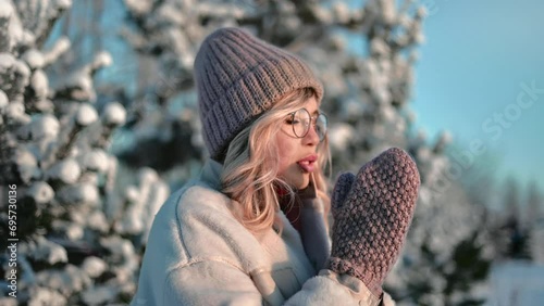 Beautiful young blonde woman feeling cold cool chill shaking mitten at winter forest snowy spruce