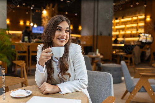 Young beautiful stylish woman in white blazer with cup of coffee. Smiling woman having coffee tea hot beverage sitting in cafe after shopping, relaxing resting alone.