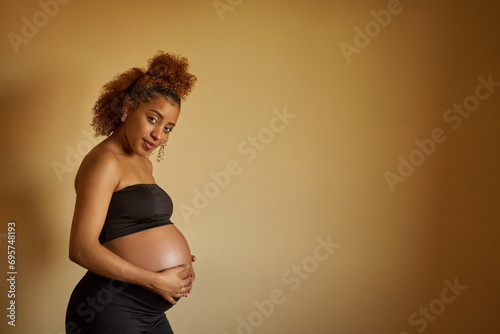 Pregnant woman looking at camera and smiling standing on isolated background. Concept of pregnancy and motherhood.