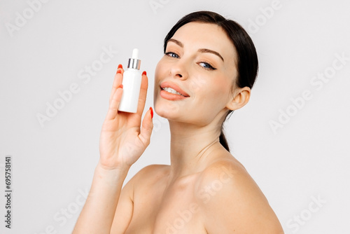 Young woman with clear glowing skin uses and holds essence in her hands on a light background. Spa care, skin care, cosmetology, creams and oils for hair and facial skin.