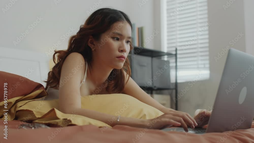 Handheld shot of freelance female manager lying in bed with laptop and answering clients messages working from home Handheld shot of freelance female manager lying in bed with laptop and answering clients messages working from home