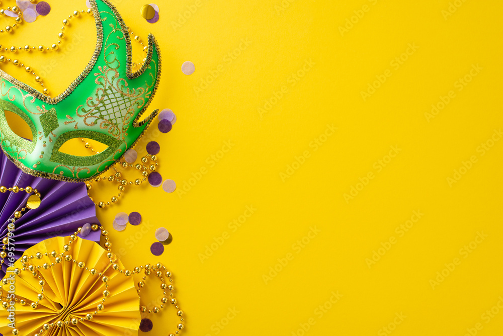 Festive Finery Arrangement: Top view capturing extravagant New Orleans mask, colorful bead strand, confetti, and decorative paper fans on a lively yellow background with space for messaging