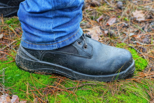 the lower part of the leg in blue stylish fashionable jeans and black lace-up leather men's fashionable warm boot with a rubber black sole on green soft moss in the forest during the winter day