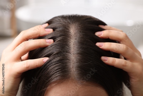 Woman examining her hair and scalp on blurred background, closeup photo