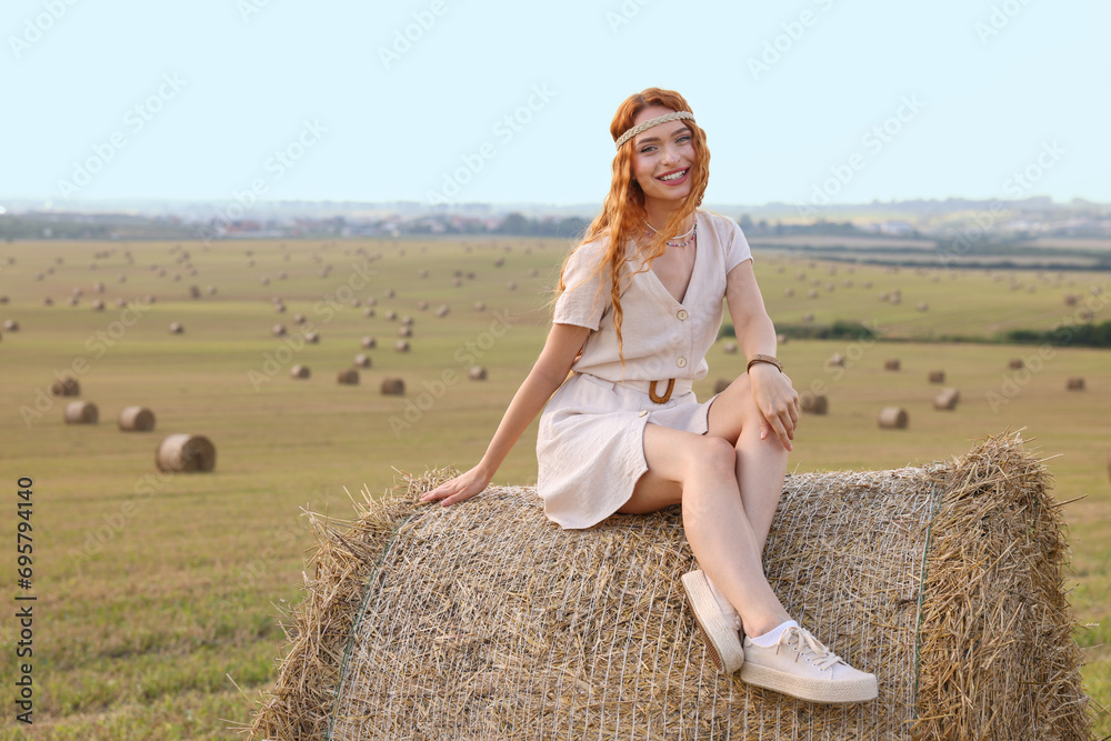 Beautiful hippie woman on hay bale in field, space for text Beautiful hippie woman on hay bale in field, space for text
