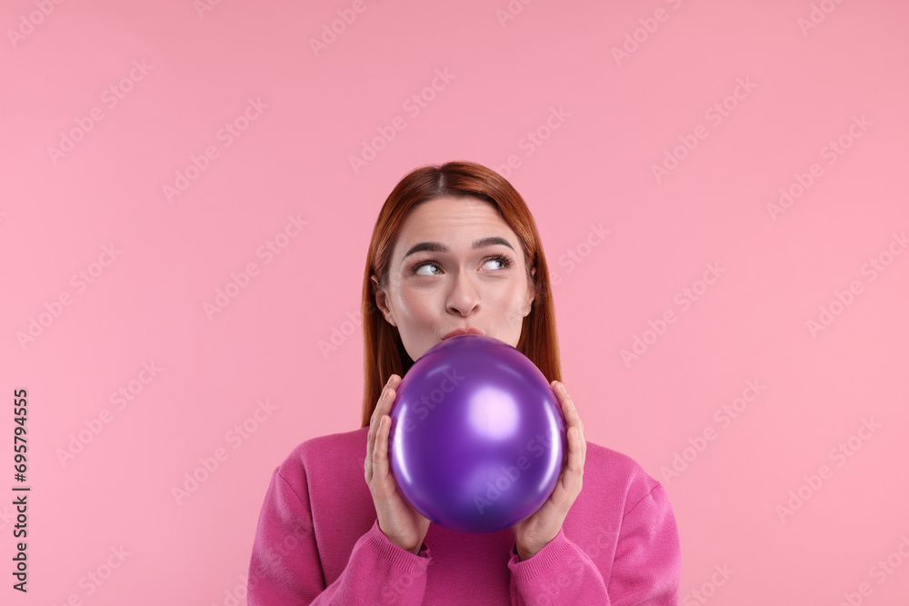 Woman inflating purple balloon on pink background Woman inflating purple balloon on pink background