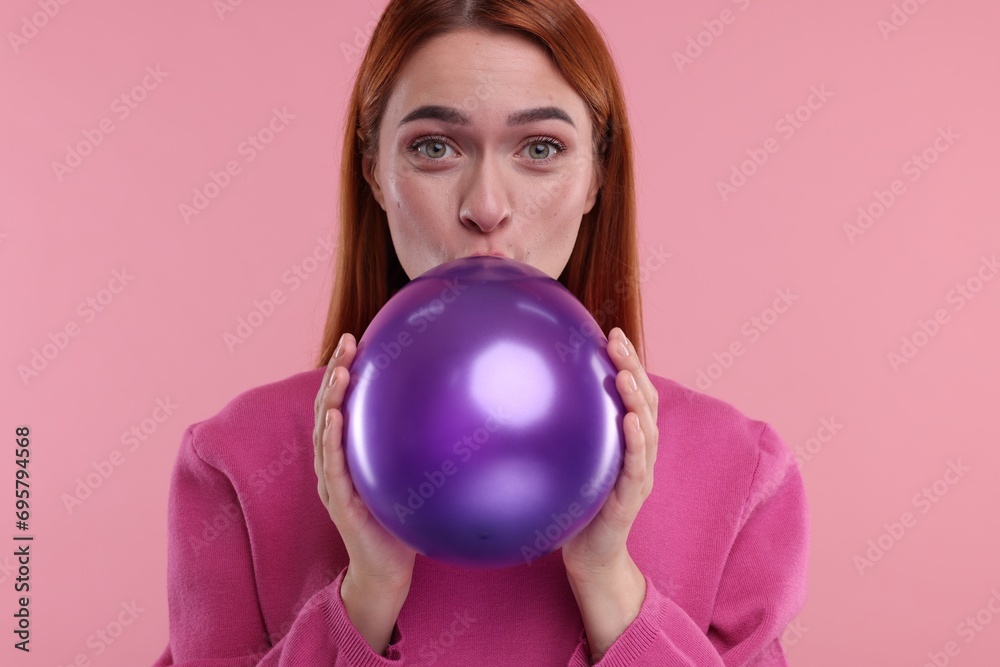 Woman inflating purple balloon on pink background Woman inflating purple balloon on pink background