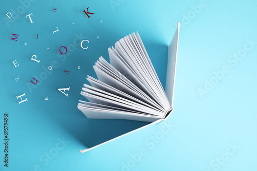 Open book with letters flying out of it on light blue background, top view photo