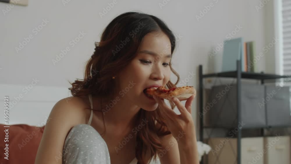 Handheld shot of female freelancer having snack break eating pizza while working or studying with laptop on bed Handheld shot of female freelancer having snack break eating pizza while working or studying with laptop on bed