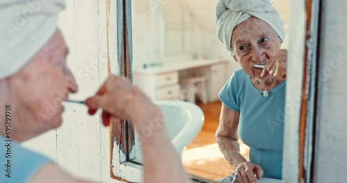 Mirror, reflection and old woman brushing teeth in the bathroom of her home for oral hygiene or dental care. Retirement, health or wellness and a senior person cleaning her mouth with a toothbrush photo