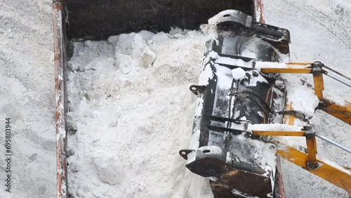 Close-up overhead above view of tractor loader machine snowplow shovel loading pile of snow and ice in dump truck for removal from city street at blizzard snowfall. Snow cleaning and removal