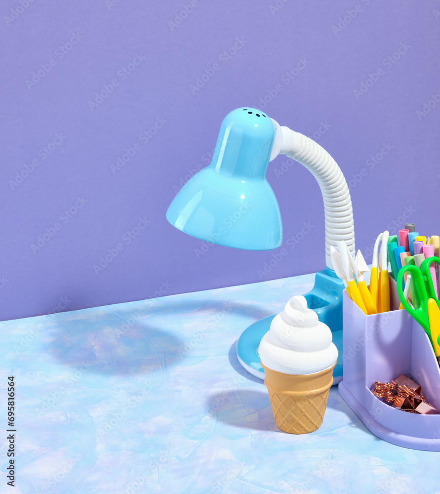 Fototapeta premium Work office table. A bright blue table lamp, a stationery stand with supplies for study and work. Fresh, cold, yummy ice cream in a waffle cup. Copy space for text.