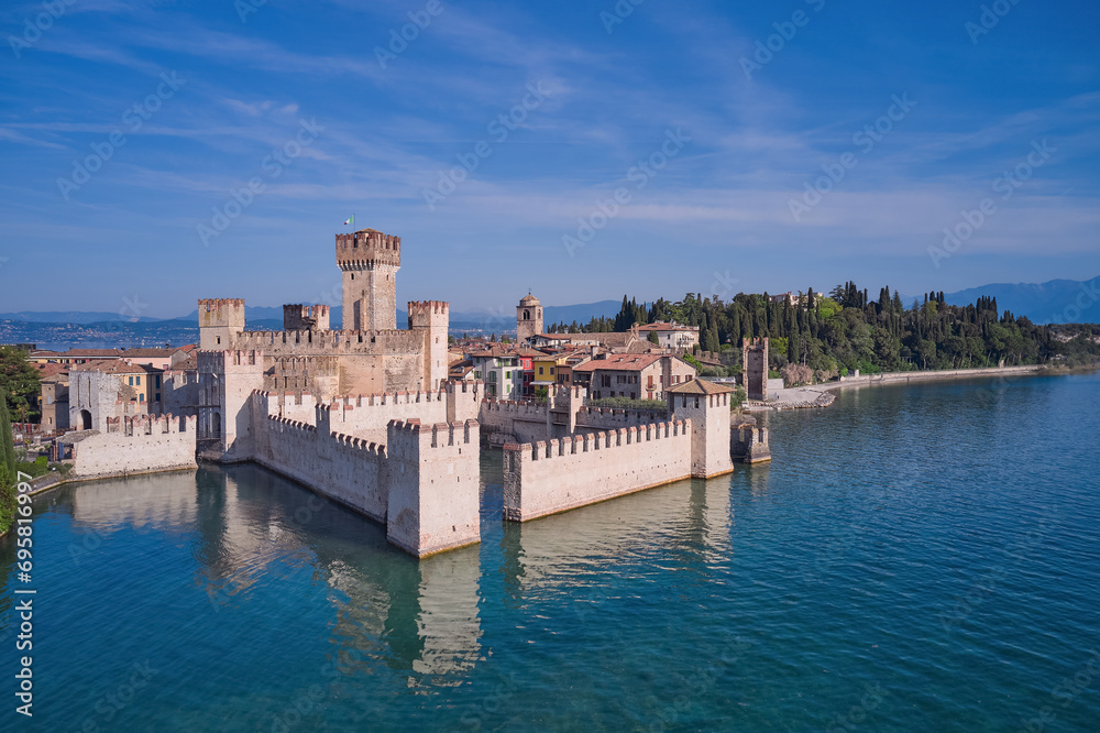Italian Scaliger Castle on the water, Sirmione. Flag of Italy on the towers of the castle on Lake Garda. Scaligero Castle drone view.