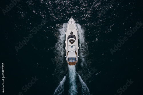 Mega large White yacht moves through dark water, top view. Large high-speed White yacht moving on dark water, aerial view.