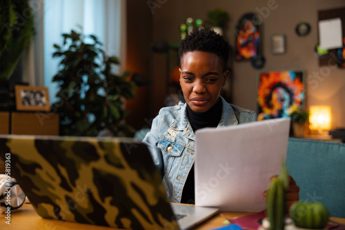 Concentrated buisness woman dark skinned girl works onlne from home observing papers education work concept. photo