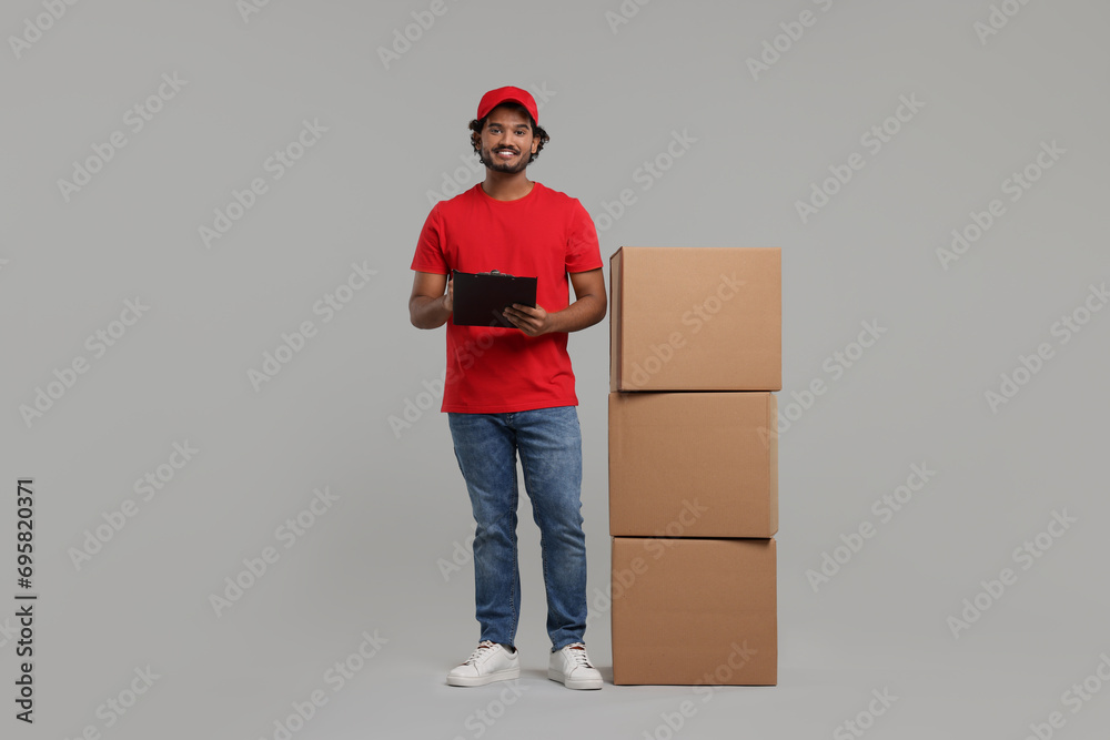 Happy courier with clipboard and stack of parcels on grey background Happy courier with clipboard and stack of parcels on grey background