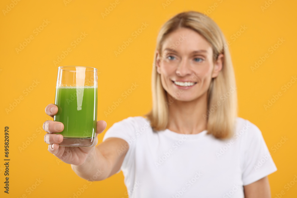 Happy woman with glass of fresh celery juice on orange background, selective focus Happy woman with glass of fresh celery juice on orange background, selective focus