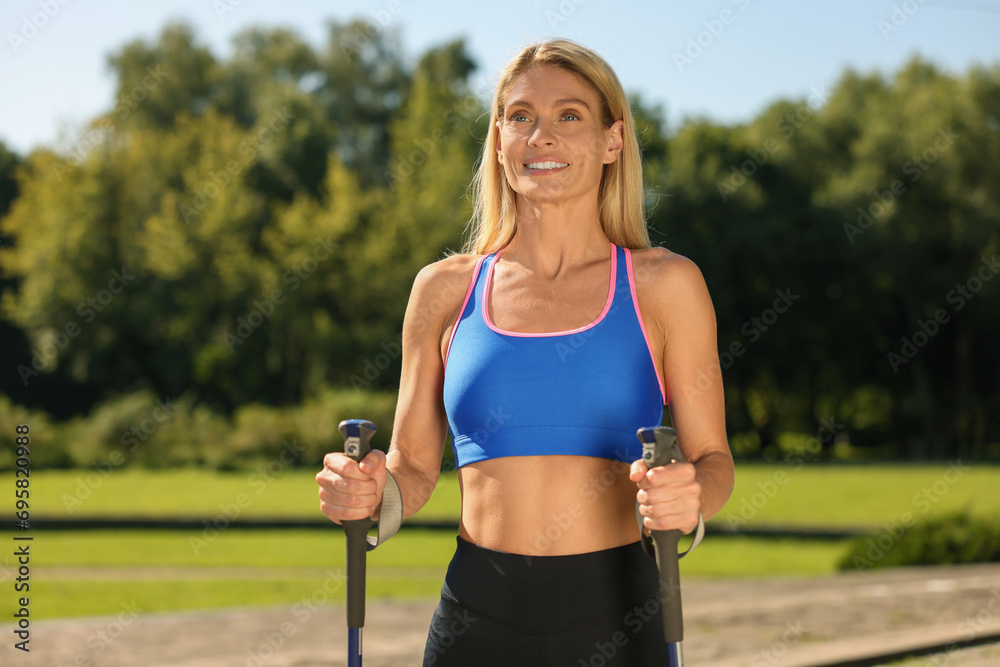 Happy woman practicing Nordic walking with poles in park on sunny day Happy woman practicing Nordic walking with poles in park on sunny day