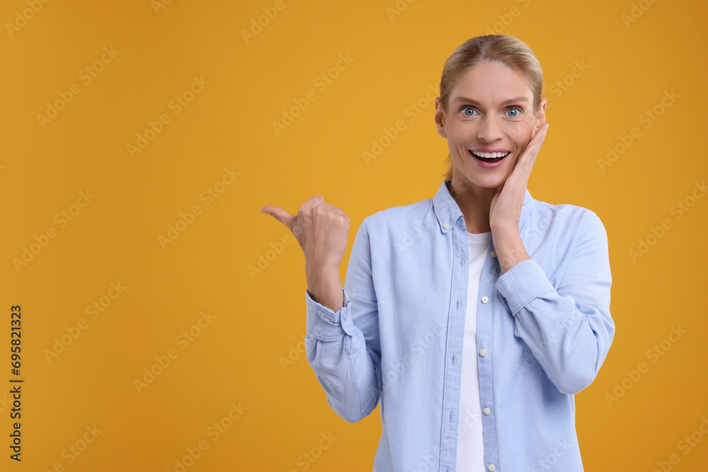 Special promotion. Smiling woman pointing at something on orange background. Space for text Special promotion. Smiling woman pointing at something on orange background. Space for text
