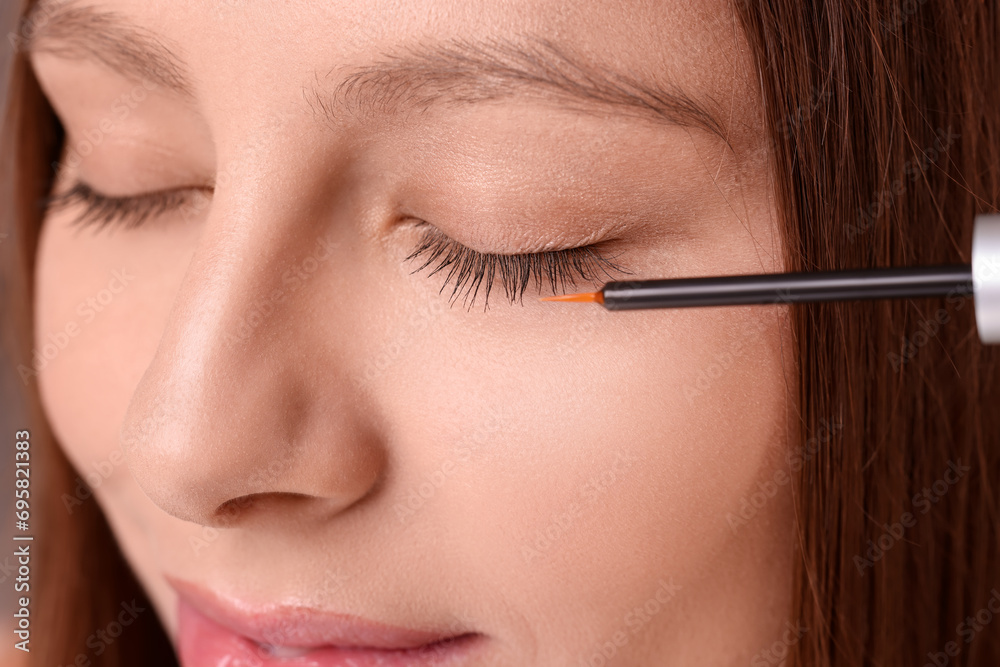 Woman applying serum onto eyelashes, closeup view