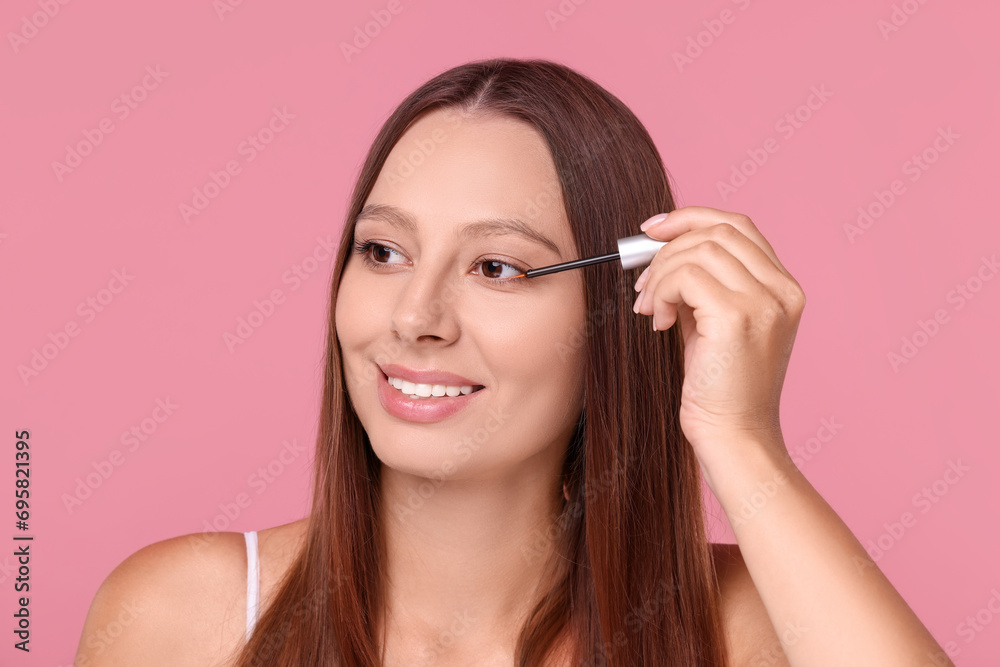 Beautiful woman applying serum onto hair on pink background Beautiful woman applying serum onto hair on pink background