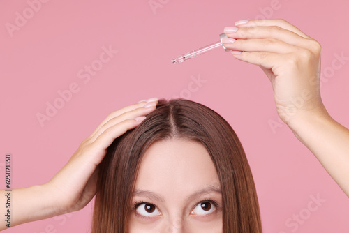 Woman applying serum onto hair on pink background, closeup