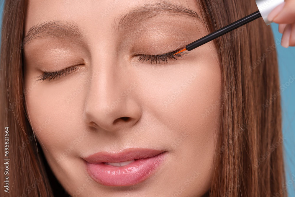 Beautiful woman applying serum onto eyelashes, closeup