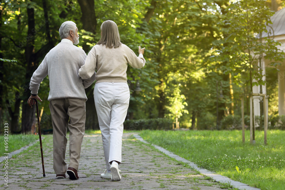 Fototapeta premium Senior man with walking cane and mature woman in park, back view. Space for text
