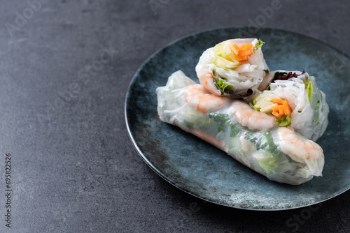 Vietnamese spring rolls with vegetables, rice noodles and prawns on black slate background. Copy space