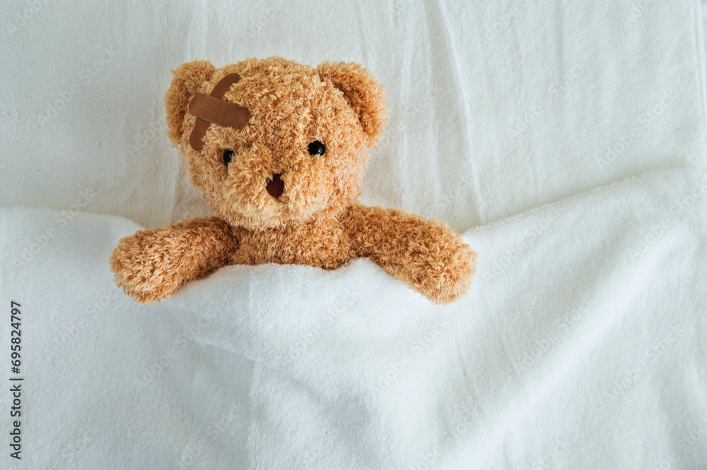Teddy bear with bandaged head ill in bed