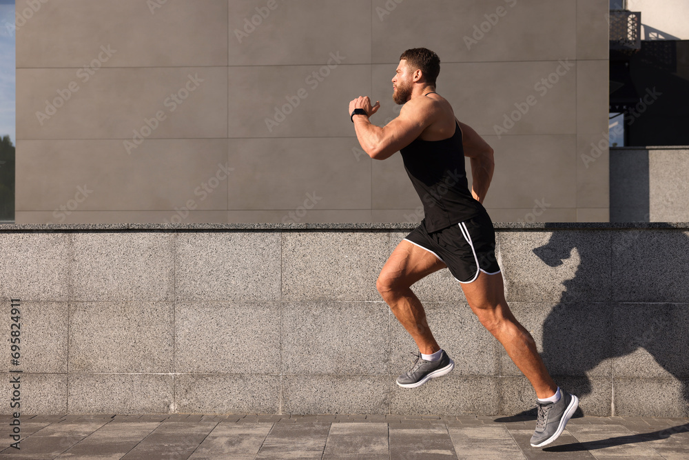 Fototapeta premium Young man running near building outdoors. Space for text