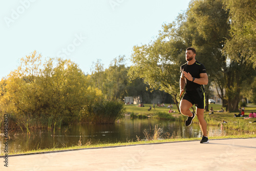 Fototapeta Naklejka Na Ścianę i Meble -  Young man running near pond in park. Space for text