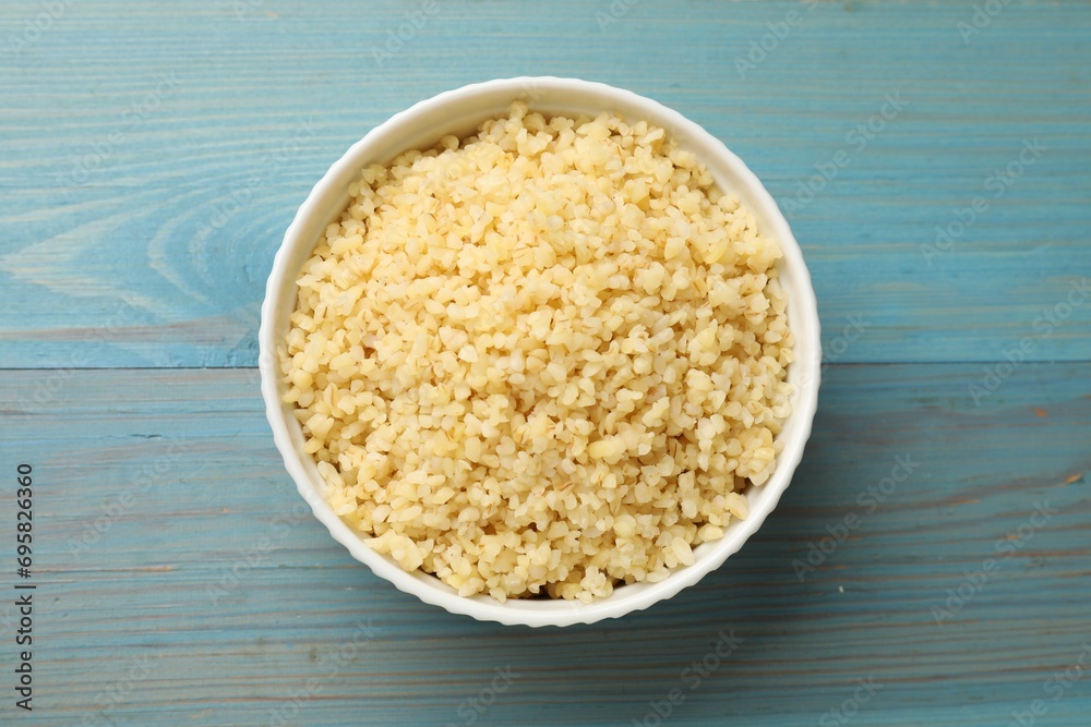 Delicious bulgur in bowl on light blue wooden table, top view Delicious bulgur in bowl on light blue wooden table, top view