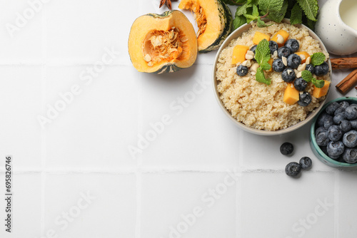 Flat lay composition with bowl of tasty quinoa porridge, blueberries and pumpkin on white tiled table. Space for text