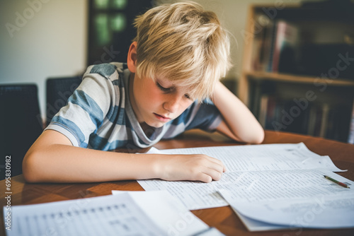 Sad tired child doing his homework sitting. The boy struggles with reading, writing and solving math problems at home. Education, school, learning disability, reading difficulties, dyslexia concept. 
 photo