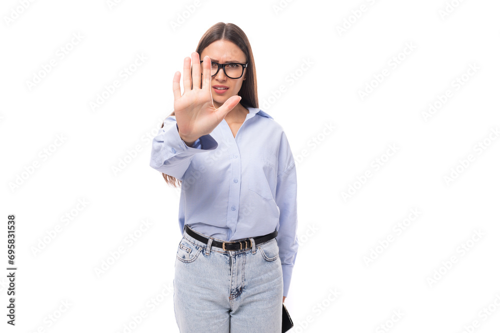 attractive well-groomed young brunette caucasian woman in glasses dressed in a sky blue shirt shows a stop gesture on a white background with copy space attractive well-groomed young brunette caucasian woman in glasses dressed in a sky blue shirt shows a stop gesture on a white background with copy space