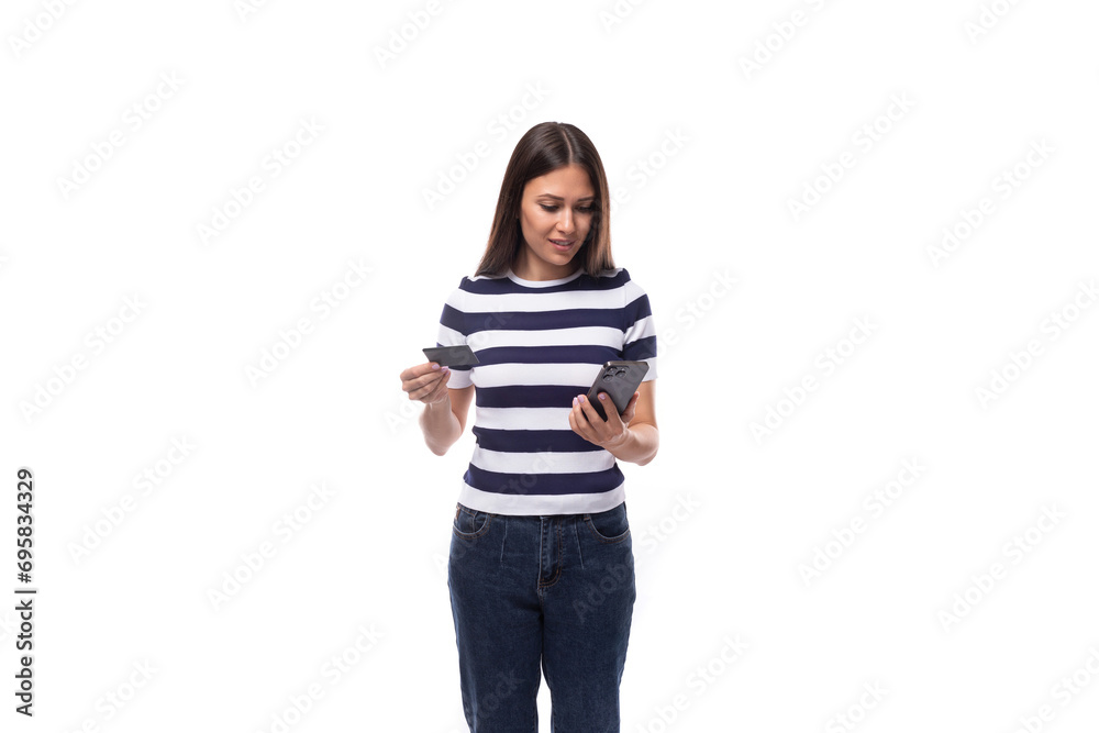 young brunette woman with straight hair dressed in a striped t-shirt holds a plastic card and a smartphone. e-business concept young brunette woman with straight hair dressed in a striped t-shirt holds a plastic card and a smartphone. e-business concept