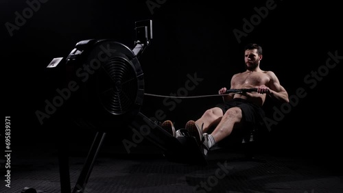 Young strong bearded bodybuilder doing a low row of rope pulleys while sitting. fitness male athlete training rowing machine exercise intense endurance training. photo