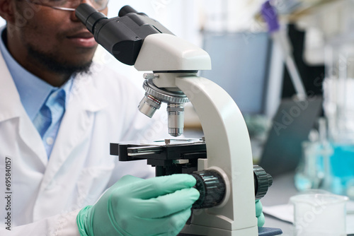 Close up shot of Black man scientist looking through microscope during scientific study, focus on microscope