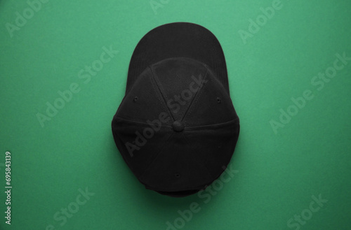 Stylish black baseball cap on green background, top view