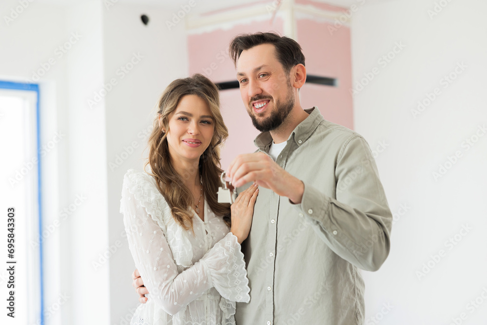 Caucasin young couple family hugging standing in the middle of new house demonstrating keys at camera sharing new appartment emitional time new first purchase rental real estate concept. Caucasin young couple family hugging standing in the middle of new house demonstrating keys at camera sharing new appartment emitional time new first purchase rental real estate concept.