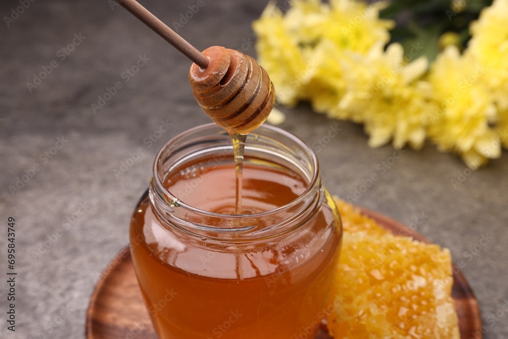 Pouring sweet golden honey from dipper into jar at grey table, closeup Pouring sweet golden honey from dipper into jar at grey table, closeup