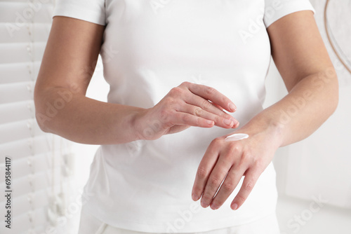 Woman applying cosmetic cream onto hand on blurred background, closeup