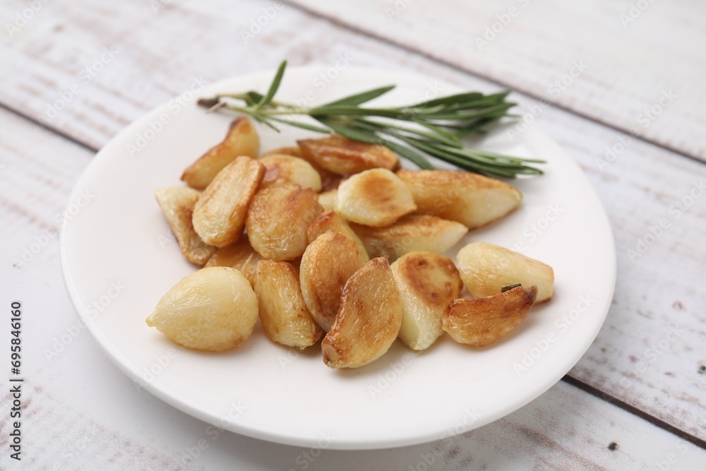 Fried garlic cloves and rosemary on wooden table, closeup