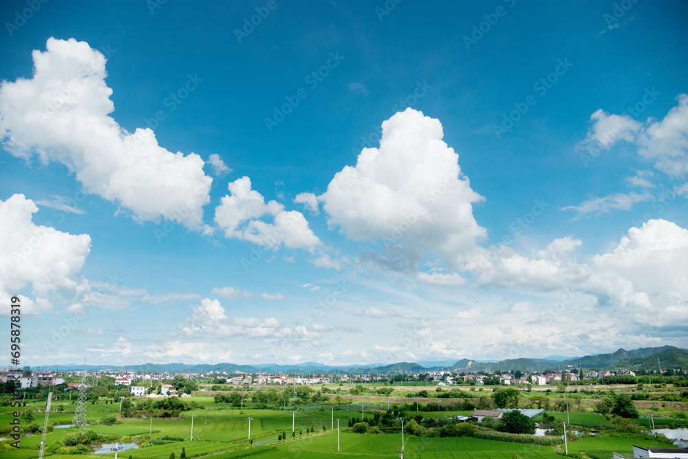 Naklejka premium Green farmland and village houses with white clouds