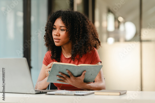 smiling African American university student with an afro hairstyle, holding a tablet and sitting at a desk with a laptop. online class learning from video conference