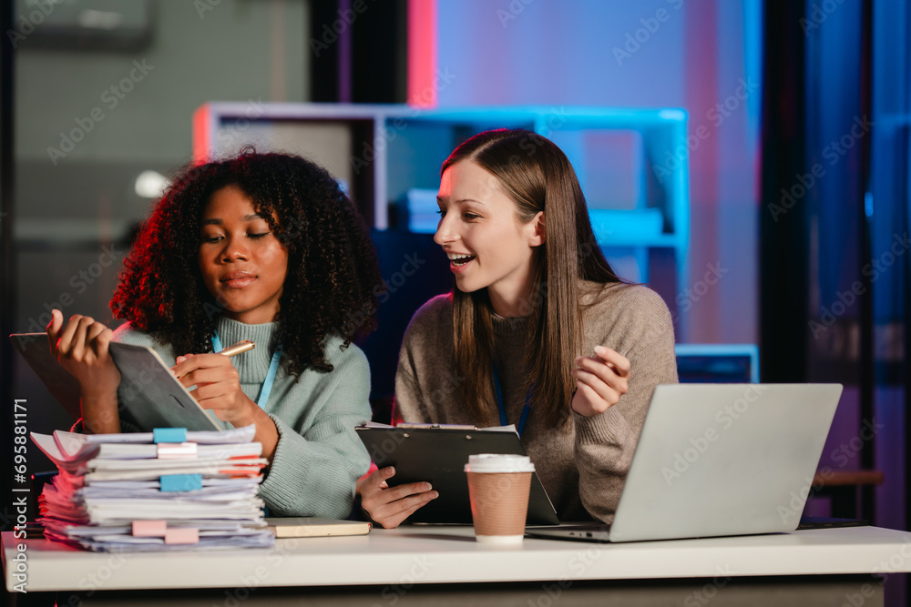 African American trainee with an afro and a Caucasian colleague working together in an office, possibly during overtime. African American trainee with an afro and a Caucasian colleague working together in an office, possibly during overtime.