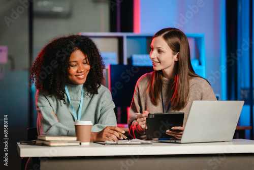 African American trainee with an afro and a Caucasian colleague working together in an office, possibly during overtime.