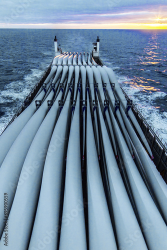 Transportation of blades for wind turbines on a cargo ship across the ocean at sunset.