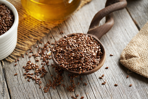 Linseeds on a wooden spoon with flax seed oil in the background